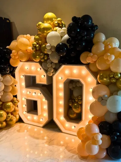 Here is a 60th milestone setup, featuring large marquee numbers surrounded by a full balloon garland in gold, black, and white. This type of decor makes a bold statement for any major anniversary or celebration.