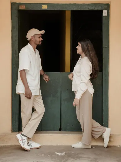 The couple stands in front of a rustic green door, their neutral outfits complementing the earthy tones of the setting.