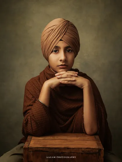 A soulful fine art portrait of a young boy in a turban. The painterly lighting and his poised expression create a powerful and timeless piece of art that captures his unique spirit.