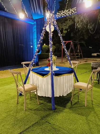 A charming table setup for four at an outdoor night event, with a blue canopy and fairy lights creating an intimate atmosphere.