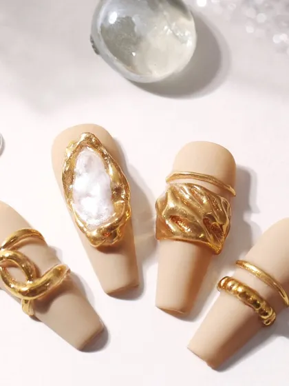 A top-down view of the gold molded nail art, highlighting the different textures and shapes, including a realistic chain link and a bezel-set stone effect.