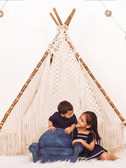 Siblings sharing a look inside a beautifully lit macrame teepee. This photo captures the special bond between a brother and sister.