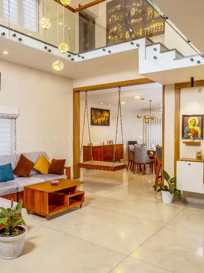 A living space that blends traditional elements with modern design. A classic wooden swing (oonjal) is paired with a contemporary sofa and a divine touch with framed pictures of Jesus.
