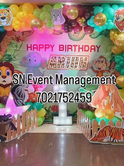 A grand jungle-themed stage decoration for Arjun's first birthday. This elaborate setup features a forest backdrop, numerous animal cutouts, a picket fence, and a light-up star prop.