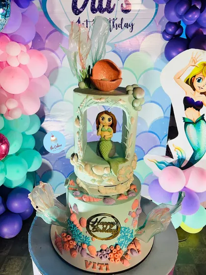 An elaborate two-tier mermaid cake with a unique 'underwater grotto' design on the top tier. This cake was the star of a mermaid-themed party, complete with a balloon backdrop.