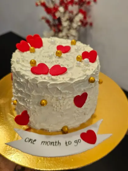 A countdown cake for a special event. This textured white buttercream bento is decorated with red and gold hearts and a banner that reads "one month to go," building excitement for a wedding or anniversary.