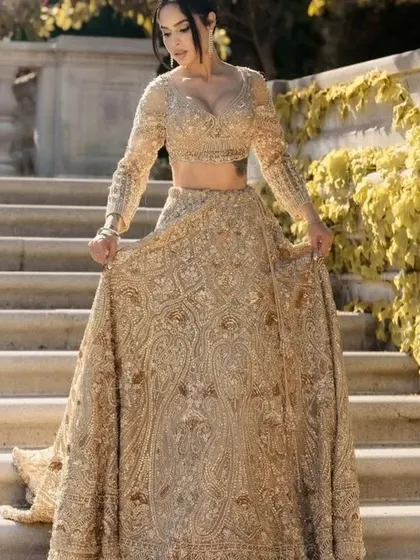 A full-length view of a stunning gold embroidered lehenga. The long sleeves and detailed work make it a regal choice for a winter wedding or a grand reception.