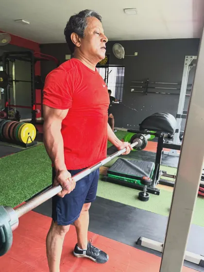 An older client performs a barbell curl, proving that age is no barrier to building and maintaining muscle strength.