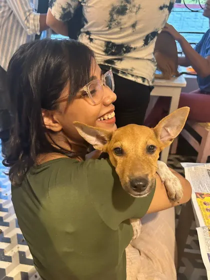 A smiling participant holds an excited indie puppy with big, expressive ears. The joy is mutual at our 'Art with Puppies' session in Kolkata.