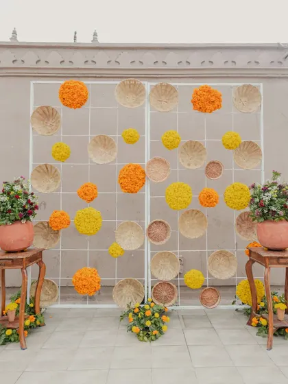 A creative and rustic photo backdrop made from a grid panel decorated with wicker baskets and spheres of orange and yellow marigolds.