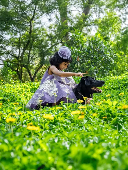 A girl pets her black Labrador in a field of flowers, a serene and beautiful moment.
