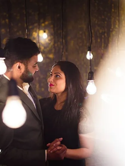 An intimate portrait of a couple surrounded by hanging light bulbs. The soft, warm light and shallow depth of field create a dreamy and romantic mood.
