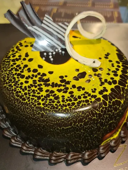A visually stunning choco-pineapple cake. This cake features a unique leopard-print effect on its glaze, created with yellow and dark chocolate.
