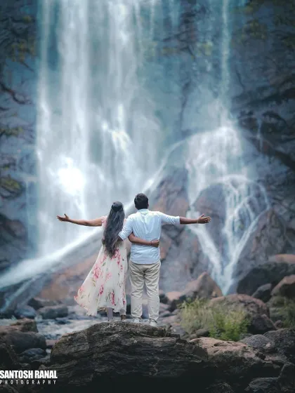 A romantic rear-view shot of a couple embracing as they look at the waterfall.