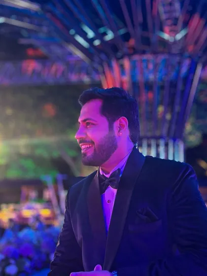A side profile shot capturing a smile during a lively Sangeet. The vibrant background lighting adds to the celebratory atmosphere.