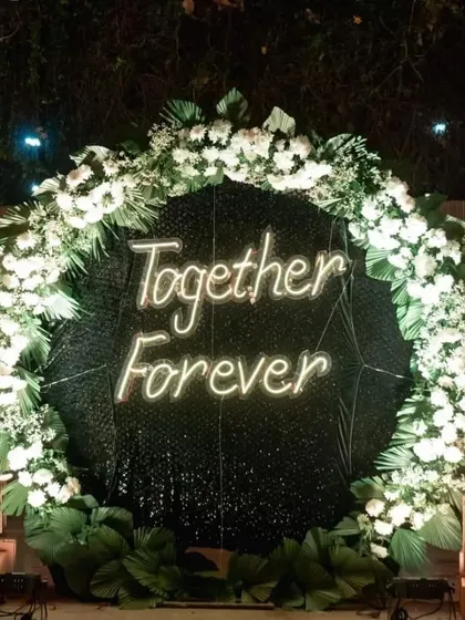 A "Together Forever" neon sign framed by a wreath of white flowers makes for a perfect selfie point at your wedding. It's a modern and romantic touch that guests will love.