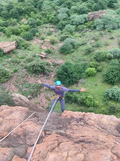 A participant joyfully rappels down a cliff, with the expansive landscape visible behind him.