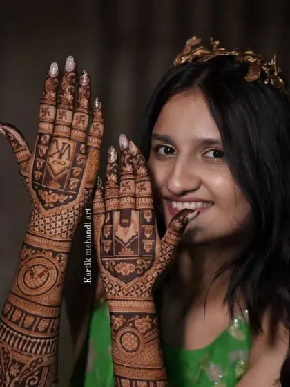 A happy bride showing her back-hand mehandi. The design features the couple's initials 'VK' and auspicious swastika symbols.