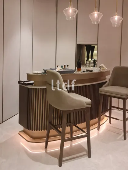 This artfully designed bar area captures attention with its fluted panels and gracefully curved form. Paired with elegant, high-backed chairs, the sleek design invites one to enjoy leisurely sips in a stylish and sophisticated setting.