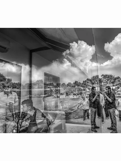 A black and white version of the gallery reflection. Stripping away the color emphasizes the forms, the clouds, and the ghostly figures, creating a more graphic and surreal composition of layered realities.