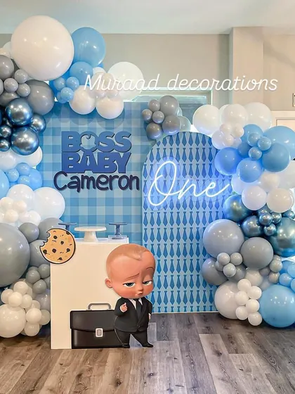 The Boss Baby theme is a huge hit for first birthdays. This setup features a custom gingham and patterned backdrop, a cool 'One' neon sign, and a life-sized character cutout, creating a playful and corporate-cute photo zone.