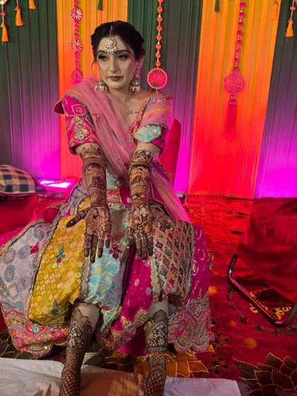 A stunning bride in her colorful mehandi outfit, showing her full bridal henna on hands and feet. The design is intricate and complements her festive look perfectly.