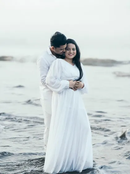 An intimate pre-wedding embrace in the ocean waves, with the groom-to-be whispering to his partner as they stand in the water.