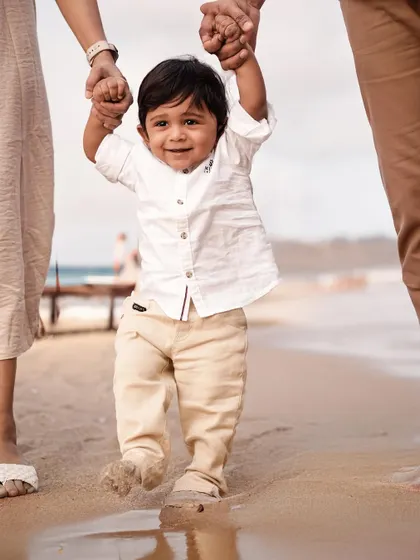 A toddler's first steps in the sand, guided by his parents. These milestone moments are priceless, and an outdoor setting makes them feel even more special.
