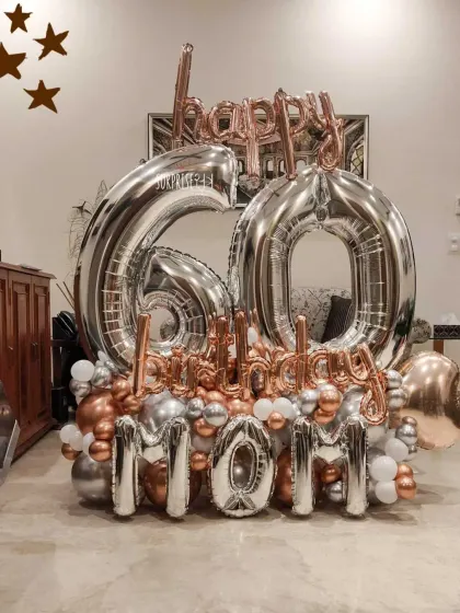 A grand balloon bouquet for a mom's 60th birthday. This arrangement features large silver foil numbers, "Happy Birthday Mom" lettering, and a base of chrome rose gold and silver balloons.