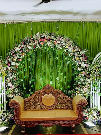 A beautiful engagement stage with a large floral arch against a green backdrop. The setup includes smaller white arches and an elegant sofa, creating a romantic and picturesque setting.