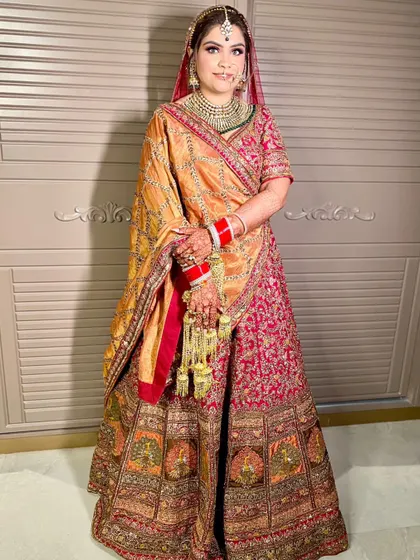 The stunning bride Sakshi in her multi-toned lehenga. The makeup features a warm, bronzed eye look that beautifully complements the orange and pink hues of her outfit.