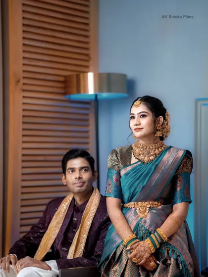 An indoor portrait of an engaged couple, highlighting the bride's stunning teal saree and gold jewelry.