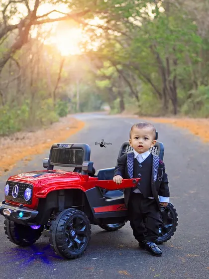 This little gentleman is celebrating his first birthday in style, looking sharp in a suit next to his cool red toy jeep.