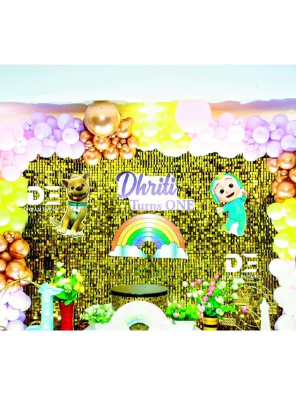 A detail from Dhriti's Cocomelon party, showing the gold sequin backdrop with a rainbow and character cutouts.