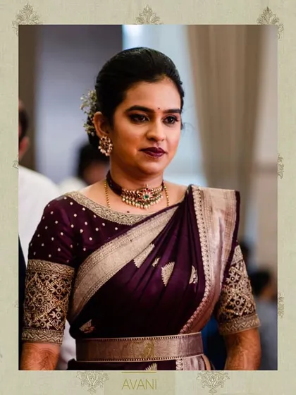 A client wearing a deep wine-colored blouse with elbow-length sleeves. The sleeves feature traditional gold embroidery, perfectly complementing her Kanchipuram silk saree.