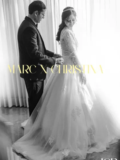 A timeless black and white portrait of the groom helping the bride with her gown.
