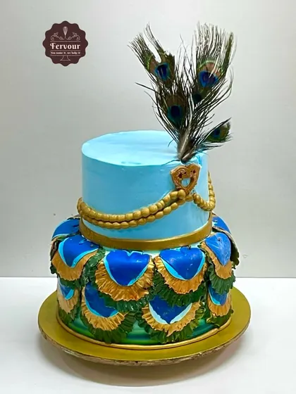 A Janmashtami special cake with a peacock theme. The design features a real peacock feather and intricate, colorful feather details made from whipped cream and chocolate.