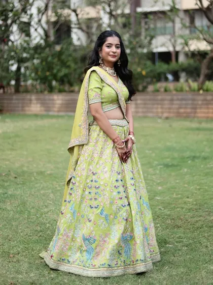 A full shot of the client in the lime green peacock lehenga, looking elegant in a garden setting.