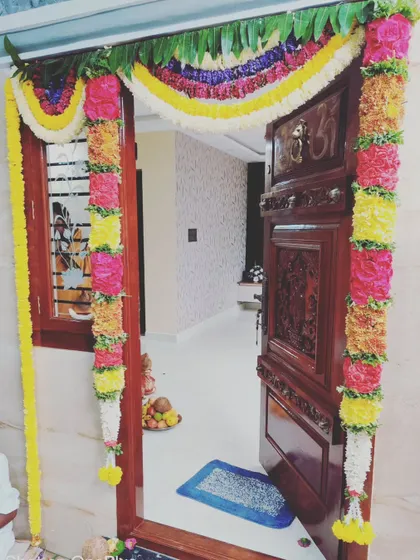 The main door decoration is key for any auspicious event. We use fresh, vibrant flowers to create these intricate garlands, framing the beautiful carved wood and setting a festive tone right from the entrance.