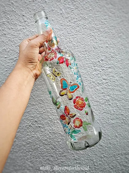 Holding the butterfly-themed glass bottle. This shows the scale of the bottle and the delicate line work of the design.