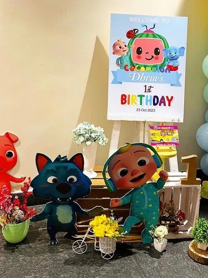 A welcome area for a Cocomelon themed party, with character standees and a personalized welcome sign on an easel.