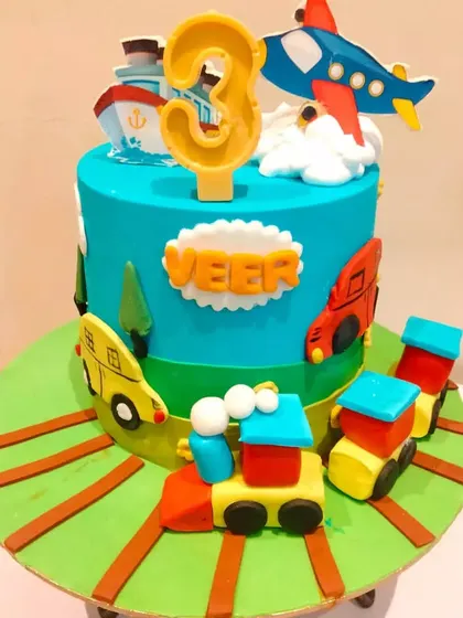 A fun transportation-themed cake for Veer's 3rd birthday, featuring a train, bus, ship, and airplane.