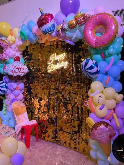 Another view of the candy-themed photo backdrop with a gold sequin wall and fun, colorful balloon sculptures.