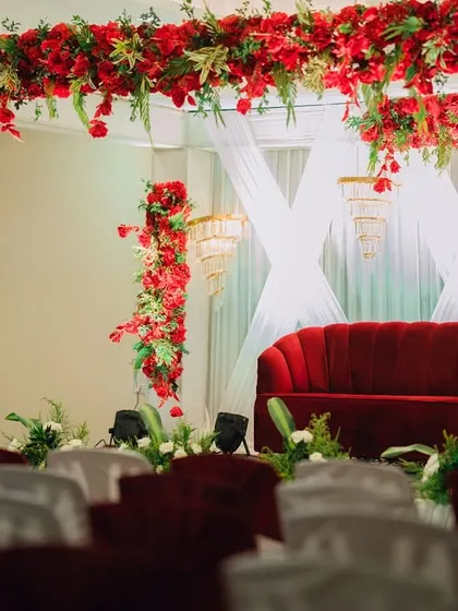 A wedding stage setup featuring a bold red sofa, lush red floral arrangements, and elegant white draping.