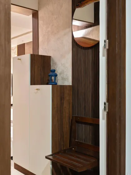 This entryway features a compact, foldable wooden chair tucked into the shoe rack unit. It provides a convenient place to sit while putting on shoes and folds away neatly to keep the foyer clear.