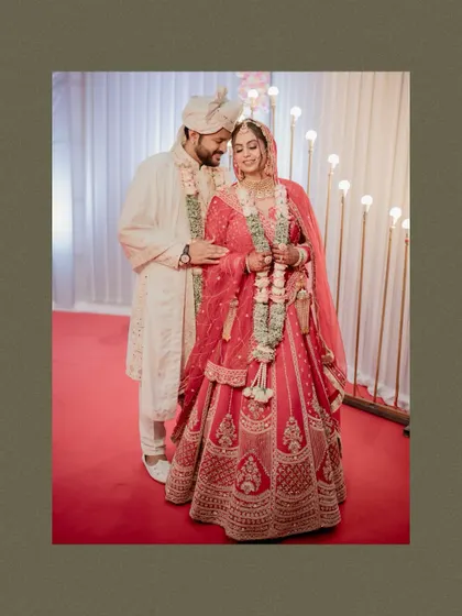 A full-length portrait of the couple at their reception, showcasing their gorgeous red and white wedding outfits.