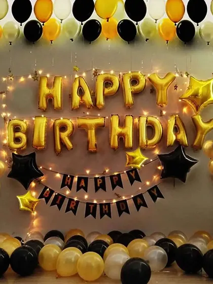 A classic black and gold birthday wall decoration with "Happy Birthday" foil letters, a banner, and fairy lights.
