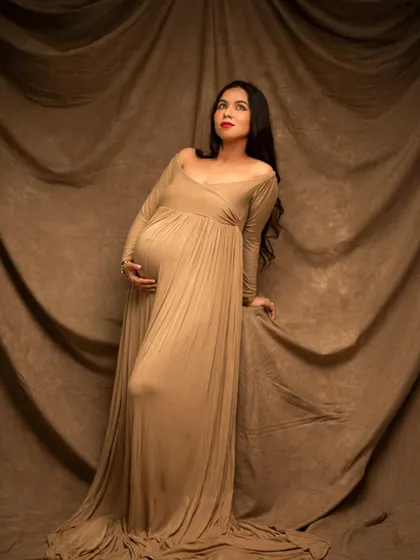 A graceful solo portrait of an expecting mother. The simple, elegant beige gown and classic studio backdrop create a timeless and sophisticated look.