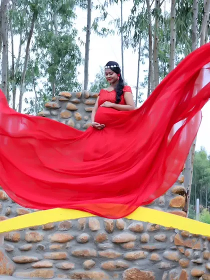 A dynamic shot of a red maternity gown with its fabric flowing in the wind, set against a backdrop of trees.