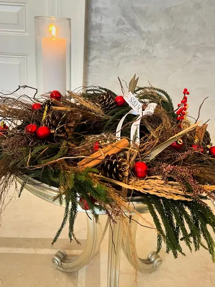 Pines, berries, and twigs come together in this rustic Christmas centerpiece. The design is built around a tall pillar candle, creating a cozy and charming decoration for a console or coffee table.